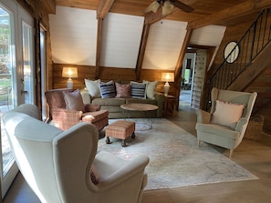Ein gemütliches Wohnzimmer mit Holztäfelung, einer Couch, Sesseln, einem Couchtisch und einer Treppe.