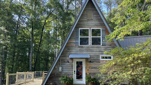 Une cabane en bois avec un toit triangulaire, une porte d’entrée et un petit porche.