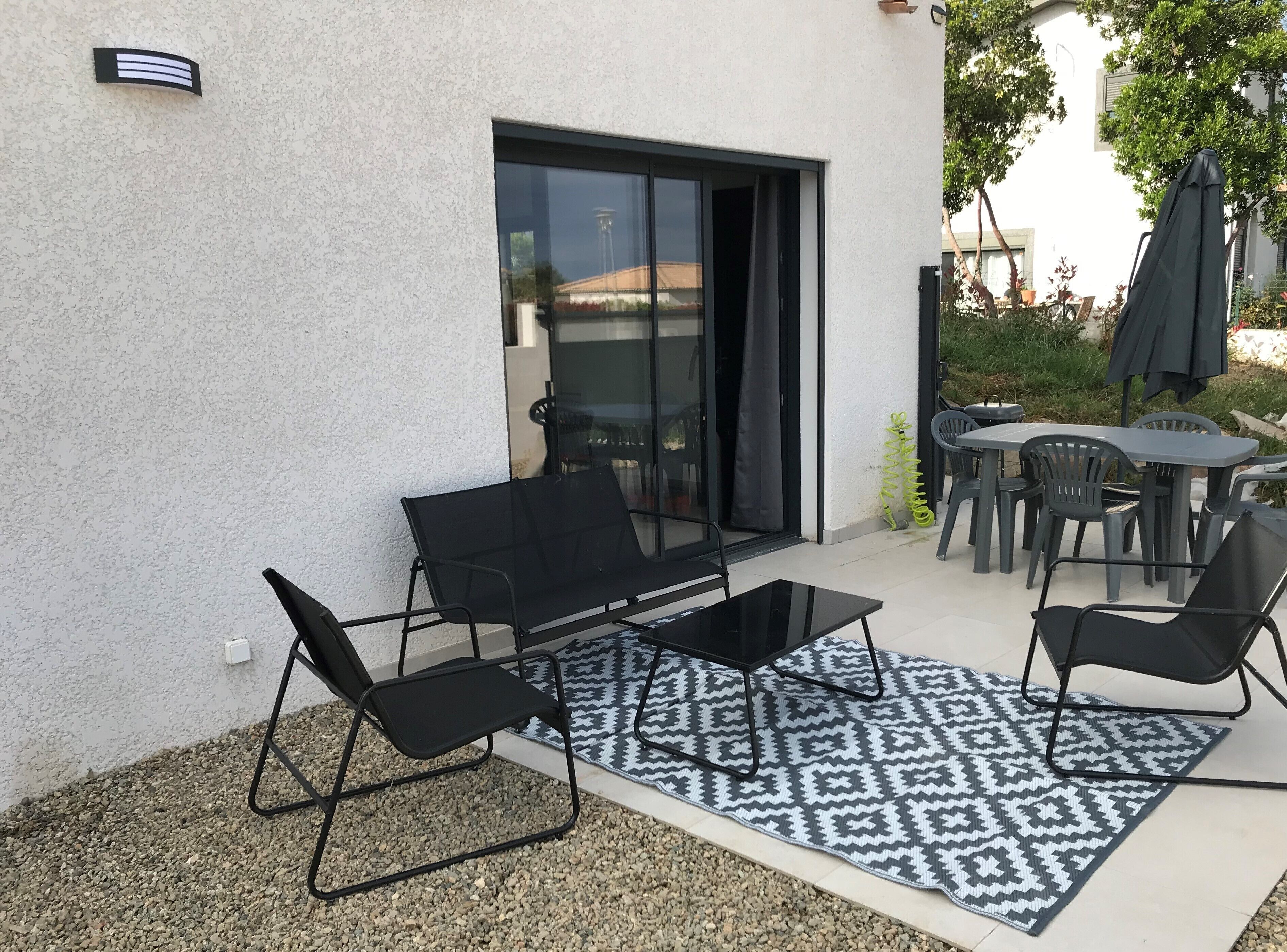 Un patio al aire libre con una mesa de metal negro, dos sillas negras y un tapete estampado.