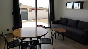 Een moderne woonkamer met een ronde houten tafel, vier zwarte stoelen, een grijze bank en een grote schuifdeur die uitkomt op een buitenruimte.