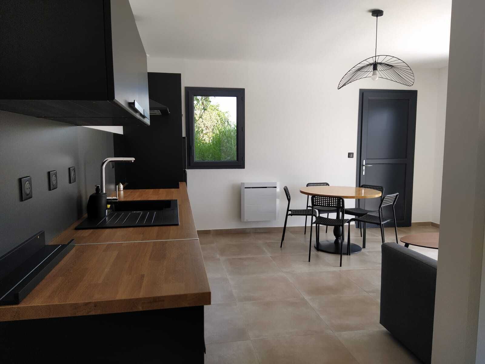 A modern kitchen with a wooden countertop, black appliances, and a dining area with a round table and chairs.