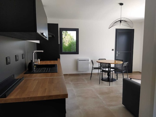 A modern kitchen with a wooden countertop, black appliances, and a dining area with a round table and chairs.