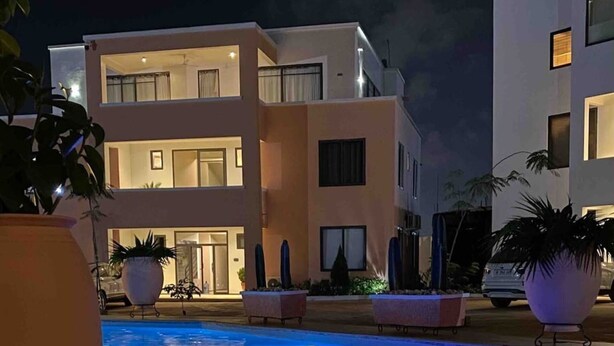 A modern building with a swimming pool at night, illuminated pool area, and potted plants. - Immaculate 2-bed Apartment at Pamv Estates Apt2 (Santeo)