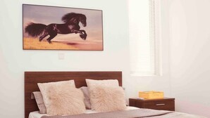 A bedroom with a wooden headboard, two fluffy pillows, a bedspread, a nightstand with a basket, and a painting of a horse on the wall. - Immaculate 2-bed Apartment at Pamv Estates Apt2 (Santeo)