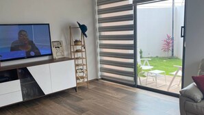 A modern living room with a flat-screen TV, a wooden ladder shelf, and a sliding glass door leading to a patio with outdoor furniture. - Immaculate 2-bed Apartment at Pamv Estates Apt2 (Santeo)