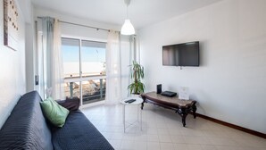 Ein modernes Wohnzimmer mit einer Couch, einem kleinen Tisch, einer Topfpflanze und einem an der Wand montierten Fernseher.