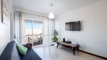 A modern living room with a sofa, a small table, a potted plant, and a TV mounted on the wall.