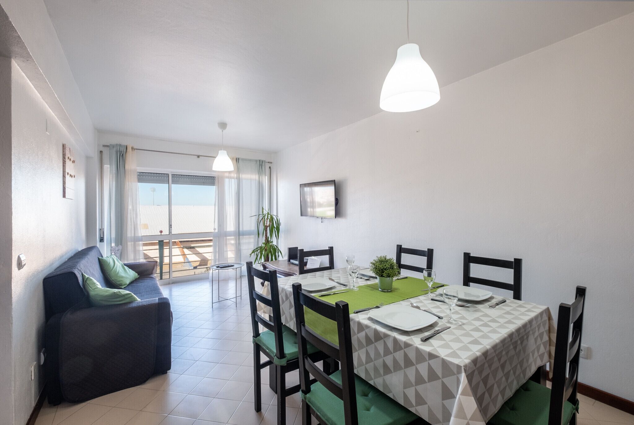 A dining area with a table set for four, green cushioned chairs, and pendant lighting.