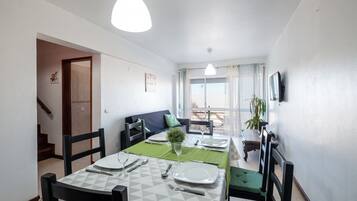 A dining area with a table set for four, a sofa, and a TV mounted on the wall.