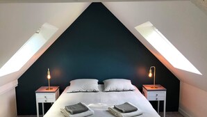 Una camera da letto con soffitto spiovente, due comodini con lampade, un letto con cuscini e asciugamani piegati sul letto.