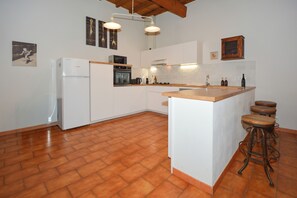 A modern kitchen with white cabinetry, a built-in oven, a refrigerator, and a wooden island with bar stools. - Townhouse near historical center of Tarascon (Tarascon)