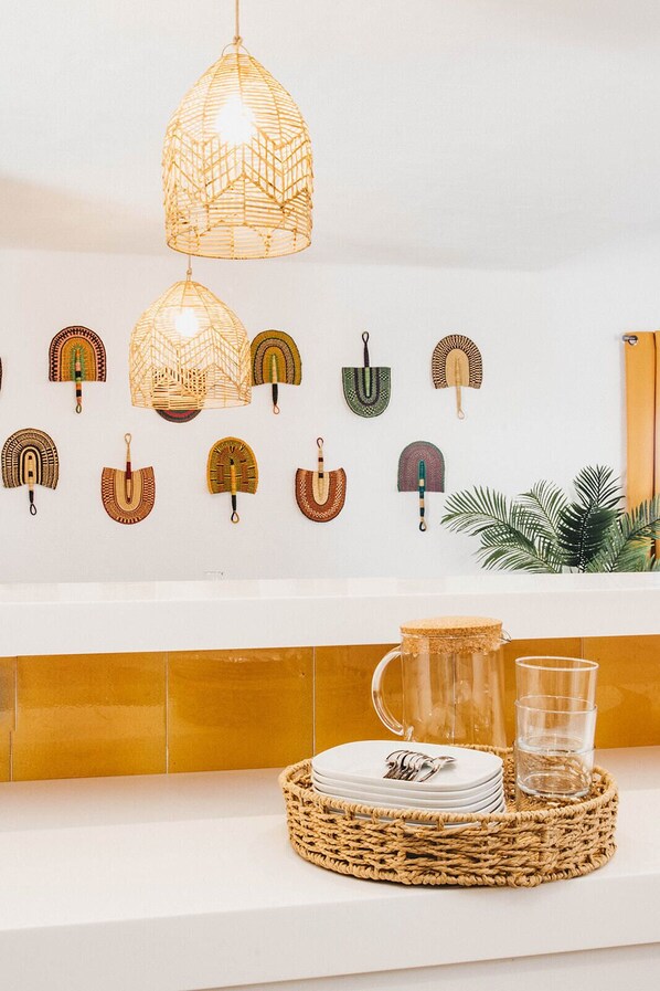 A kitchen with a white countertop, a woven basket with plates and cutlery, a glass pitcher, and a hanging light fixture.