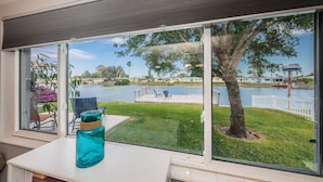 A room with a large window overlooking a lake, a grassy area, and a dock. - Serene Lakefront home in Tampa Bay, close to beaches and downtown Tarpon Springs (holiday)