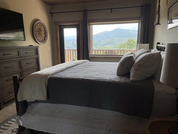 Une chambre dotée d’un grand lit, d’une commode, d’un téléviseur à écran plat et d’un balcon offrant une vue sur les montagnes.