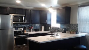 A modern kitchen with dark cabinets, stainless steel appliances, a central island with stools, and a window providing natural light.