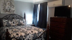 A bedroom with a bed, a dresser, a television, and a window with curtains.