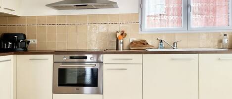 A modern kitchen with a built-in oven, a coffee maker, and a window with lace curtains.