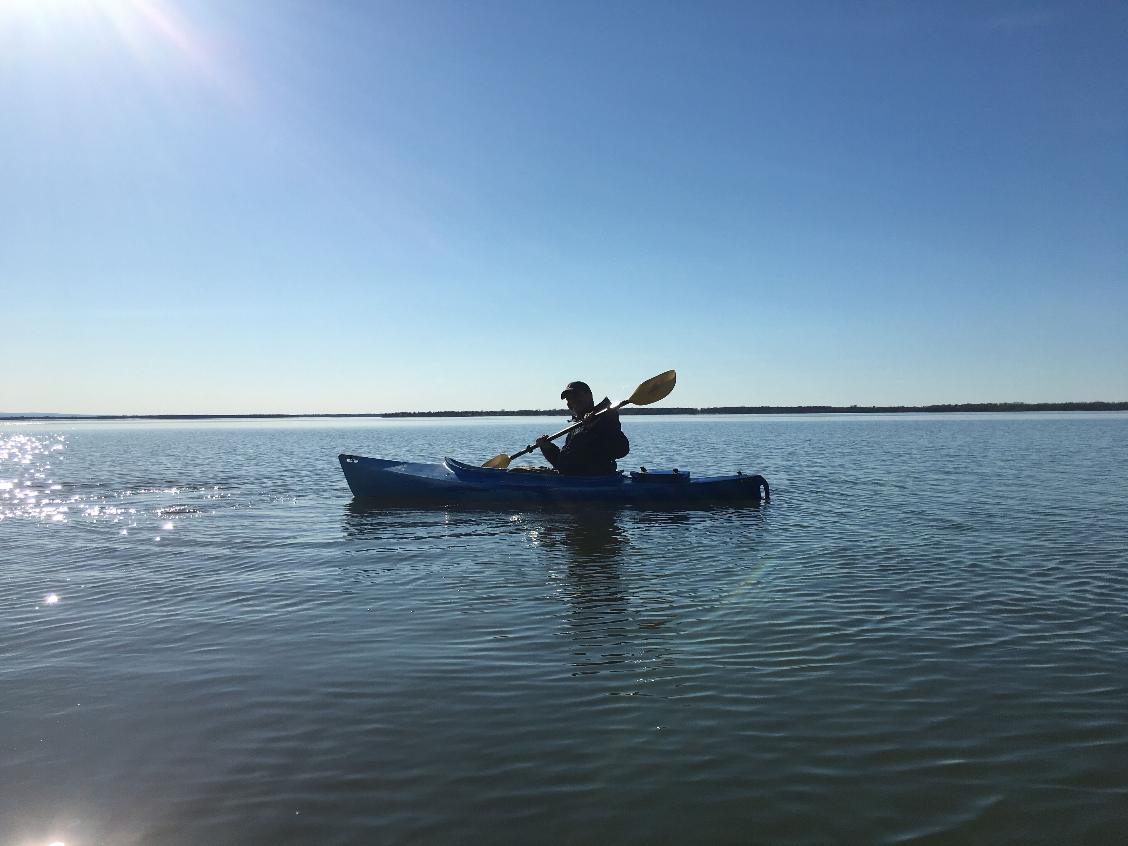 Una persona practica kayak en aguas tranquilas bajo un cielo despejado.