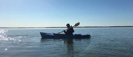 Una persona practica kayak en aguas tranquilas bajo un cielo despejado.