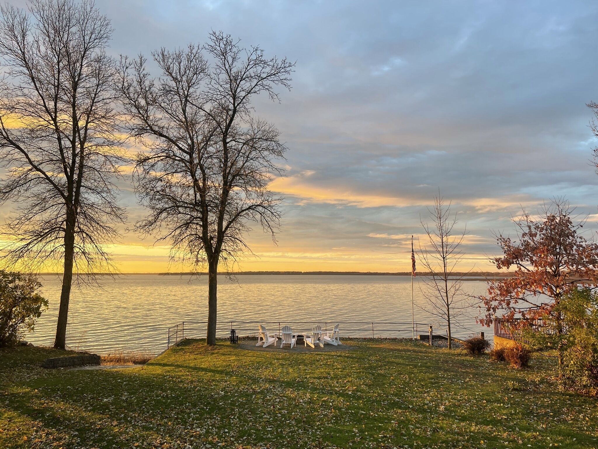 Une vue sur le lac, avec des arbres et une rangée de chaises blanches disposées face à l’eau.
