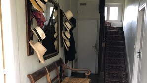 Een gang met een houten bank, een spiegel en een verzameling hoeden aan de muur.