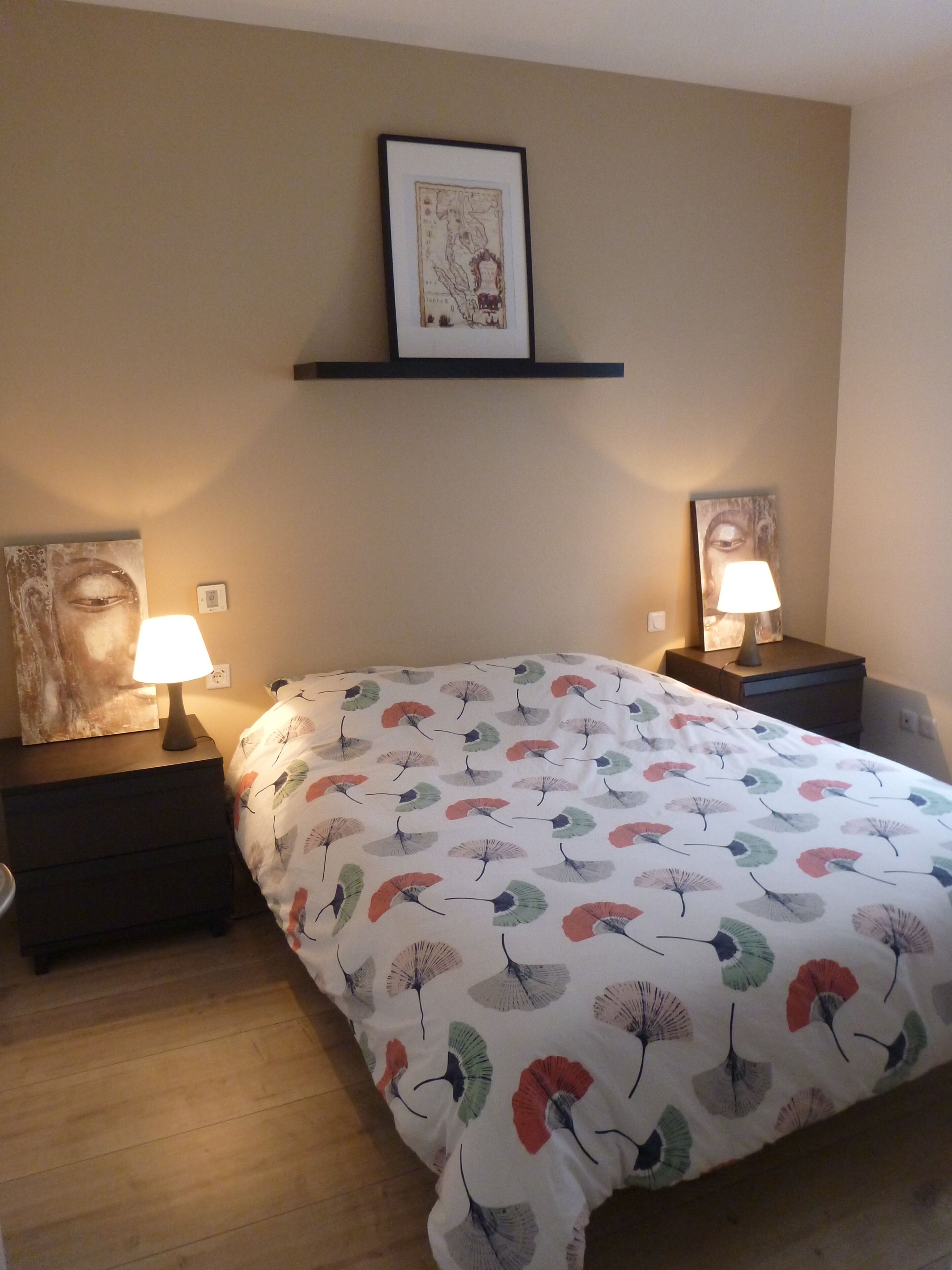 Une chambre à coucher avec un lit, deux tables de chevet avec des lampes, un tableau encadré au mur et une couvre-lit à motifs.