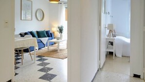 A modern living room with a blue sofa, a white coffee table, and a dining area with a white table and chairs. - Beau T3 -terrasse & Parking, Proche Plage 1er Étage Droite (Hyères)