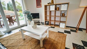 A living room with a white table, a TV, a bookshelf, and a large window. - Beau T3 -terrasse & Parking, Proche Plage 1er Étage Droite (Hyères)