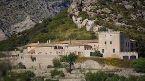 A coastal building with a stone wall, multiple windows, and a tower. - Apartamento Coral, Holiday Apartment in Puerto Pollença (Puerto Pollença)