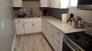 Een moderne keuken met witte kastjes, een granieten aanrechtblad, een roestvrijstalen fornuis en een koffiezetapparaat.