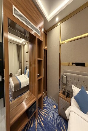 A hotel room with a large mirror, a bed with blue and white bedding, a tufted headboard, a bedside table with a lamp, and a blue patterned carpet. - Holiday Al Khaleej Hotel (Al Khobar)