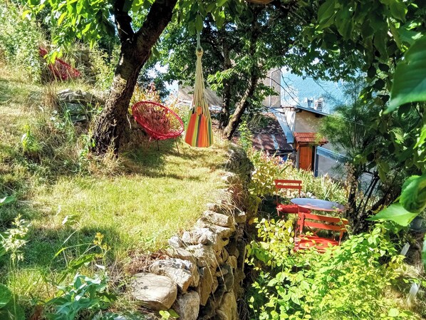 A garden with a stone wall, a red chair, a table, and hanging decorations.