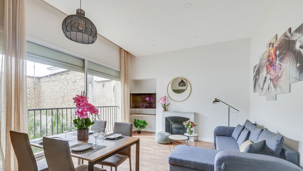 A modern living room with a dining area, a grey sofa, a fireplace, and a balcony with a view of a stone wall. - 4bed/4bath, Luxury AND Calm, 10min Walk From Beach (Cannes)