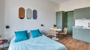 A modern bedroom with a bed, a small table with fruits, a chair, and a kitchenette area. - 4bed/4bath, Luxury AND Calm, 10min Walk From Beach (Cannes)