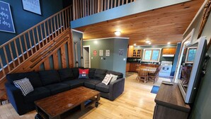 A spacious living area with a large black sectional sofa, a wooden coffee table, and a kitchen in the background. - "Dingle Run Lodge" at Sir Sam's (hot tub/sauna) (EAGLE)