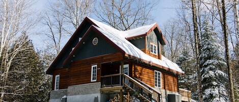 A log cabin with a balcony, surrounded by snow-covered trees.