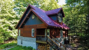A cabin with a steeply pitched roof, a wooden exterior, and a stone foundation. It features a front porch with a staircase leading to a deck. - "Dingle Run Lodge" at Sir Sam's (hot tub/sauna) (EAGLE)
