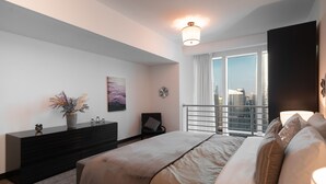 Een moderne hotelkamer met een groot bed, een donkere houten dressoir, een stadszicht door het raam en een skyline buiten.