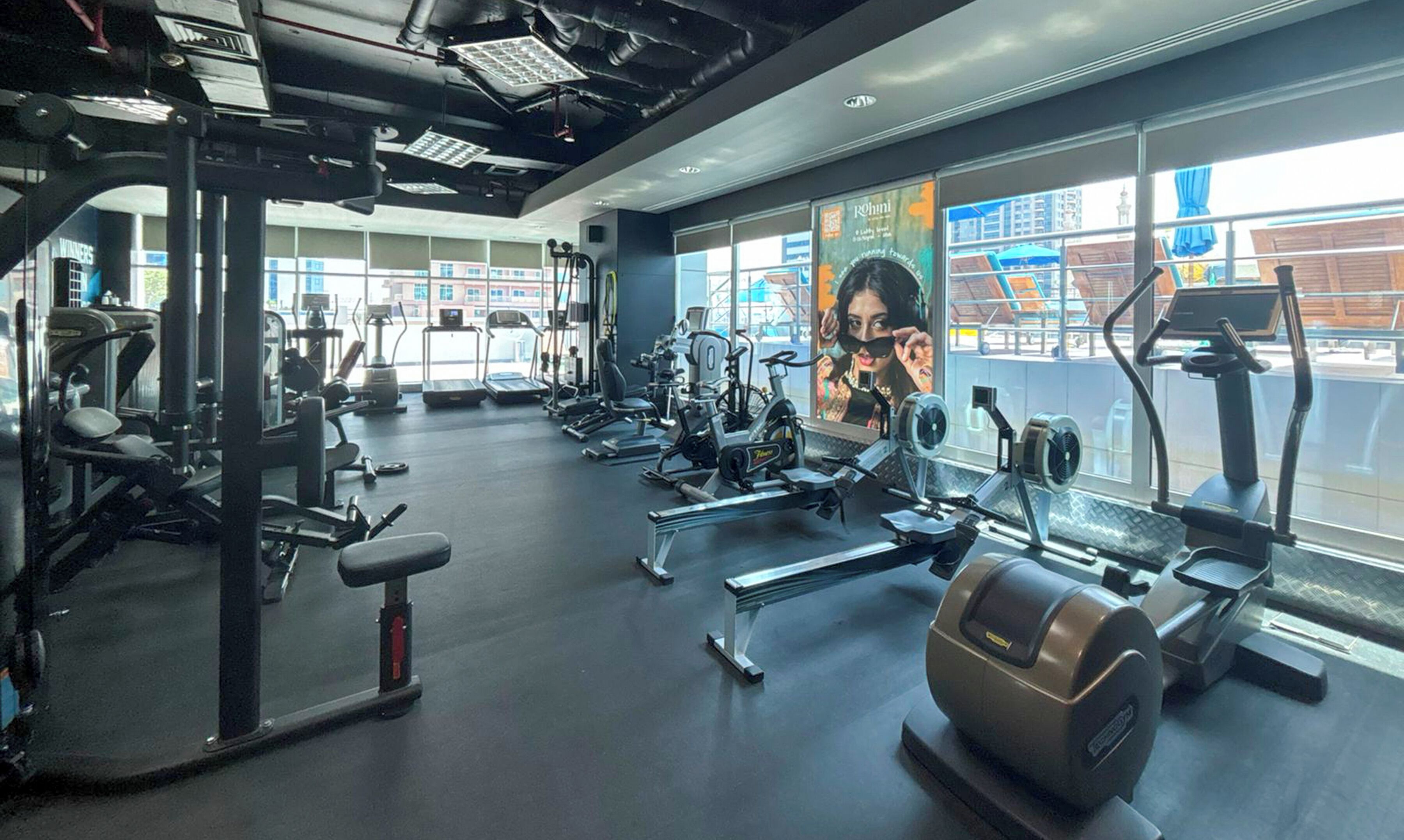 A gym with various exercise equipment, large windows, and a view of the outside.