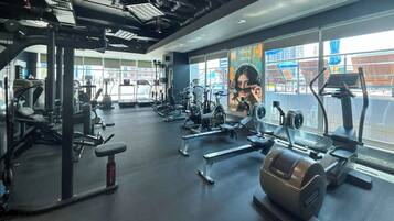A gym with various exercise equipment, large windows, and a view of the outside.