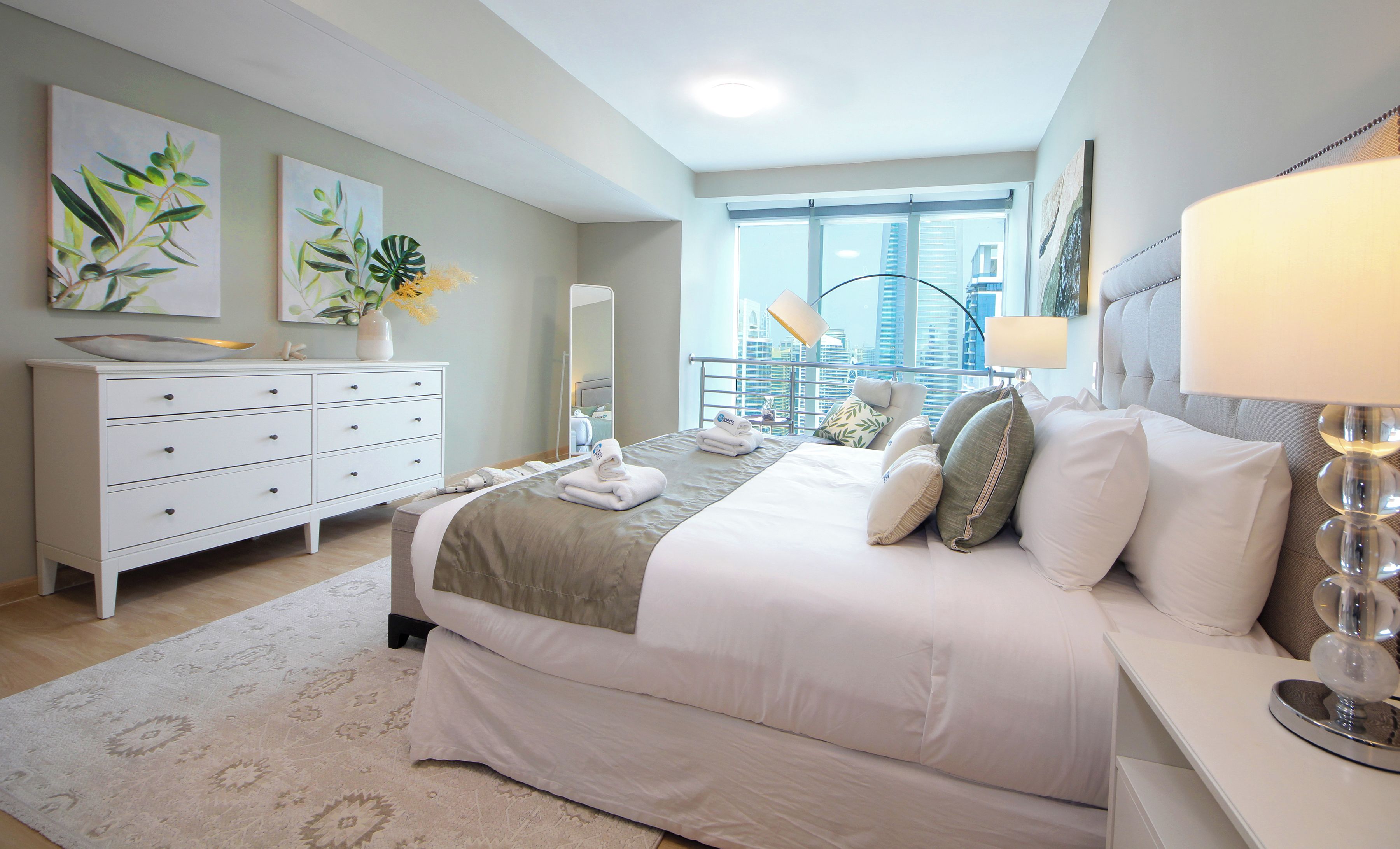 Een moderne hotelkamer met een groot bed, een witte dressoir, een spiegel en uitzicht op de stad.