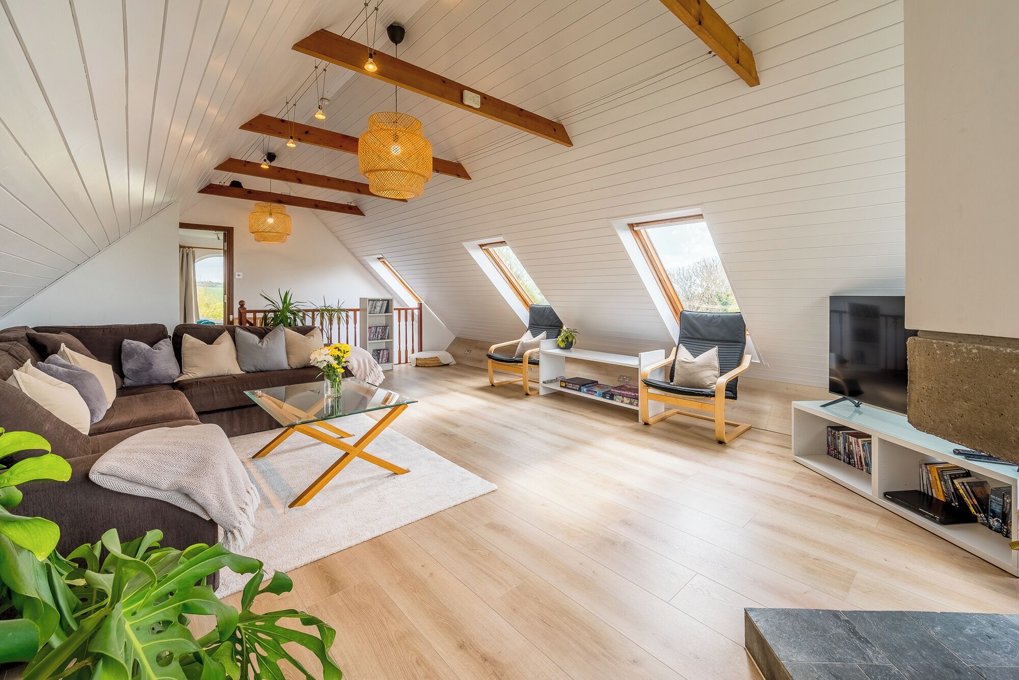 A spacious loft with a high ceiling, wooden beams, and large windows.