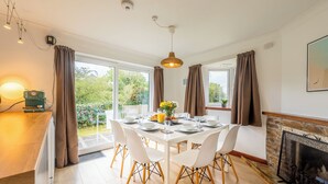A dining area with a table set for four, white chairs, a vase with flowers, and a view of greenery outside. - Peaceful countryside retreat with sea views (Penzance)