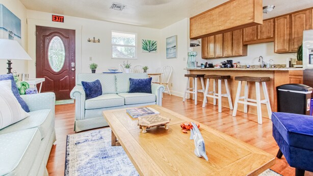A living room with a sofa, coffee table, and a kitchen area with wooden cabinets and a bar stool. - Spacious two-bedroom apartment with private, heated pool (near beaches) (St. Petersburg)