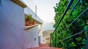 Una escala que condueix a un balcó amb plantes en testos i vista al mar.