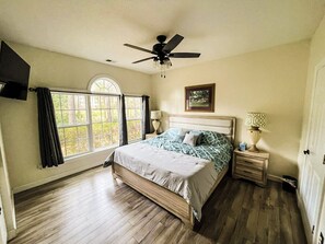 Ein Schlafzimmer mit einem Bett, Deckenventilator, Fenster und Nachttisch mit Lampe.