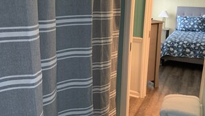 Une chambre avec un lit, une table de chevet, une lampe et une salle de bain avec des rideaux à rayures.
