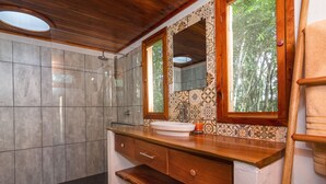 Ein Badezimmer mit einem Holzkosmetikschrank, einem großen Spiegel und einer Duschkabine.