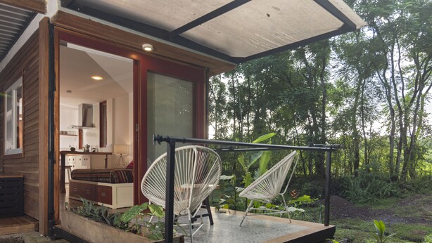Eine moderne Terrassenanlage mit zwei weißen Drahtstühlen, einer Steinstufe und Blick auf einen üppigen Garten.