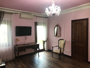 Une pièce comprenant un bureau en bois, une chaise, un téléviseur, un miroir et un lustre.